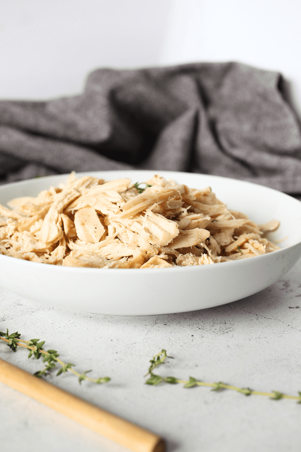 front view of a bowl of quick pulled chicken recipe with fresh herbs and a wooden spoon