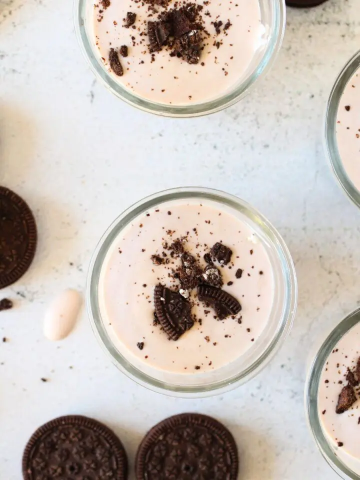 homemade keto probiotic protein yogurt made with cookies and cream protein powder and crushed keto cookies. Additional keto cookies are scattered around gold spoons