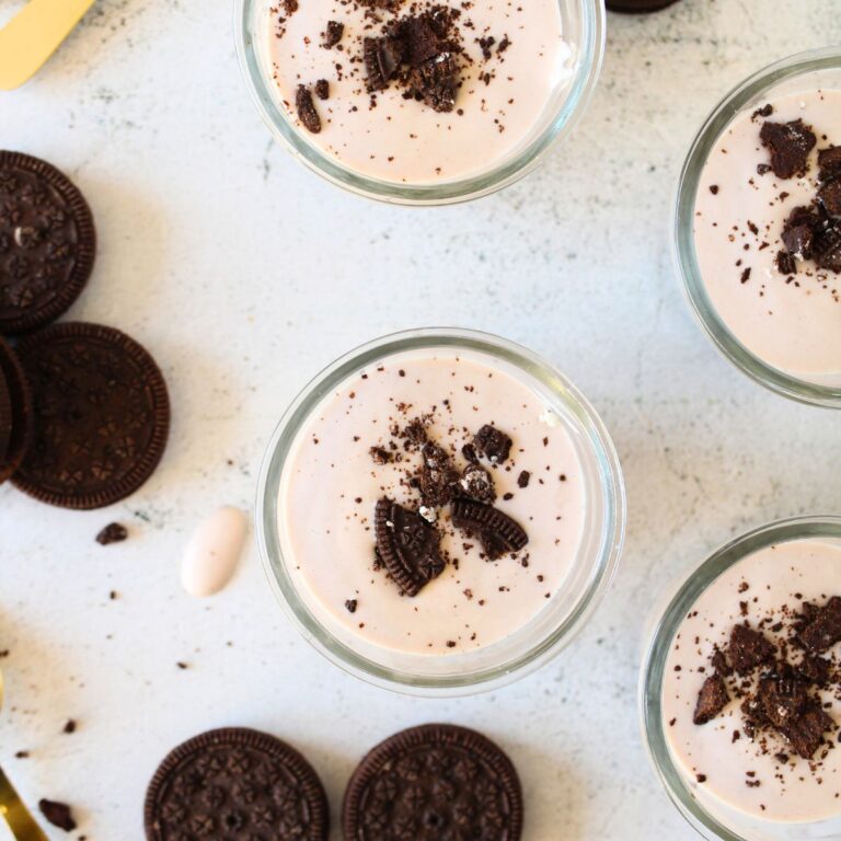 homemade keto probiotic protein yogurt made with cookies and cream protein powder and crushed keto cookies. Additional keto cookies are scattered around gold spoons