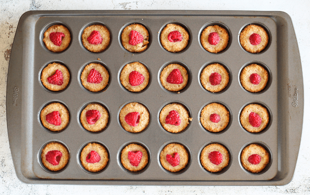 top view of mini muffin pan with baked keto raspberry Financier cookies that are just brown on the edges