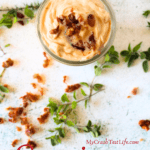 a jar filled with homemade keto carnivore bacon mayo with a spoon in the jar and fresh herbs scattered around