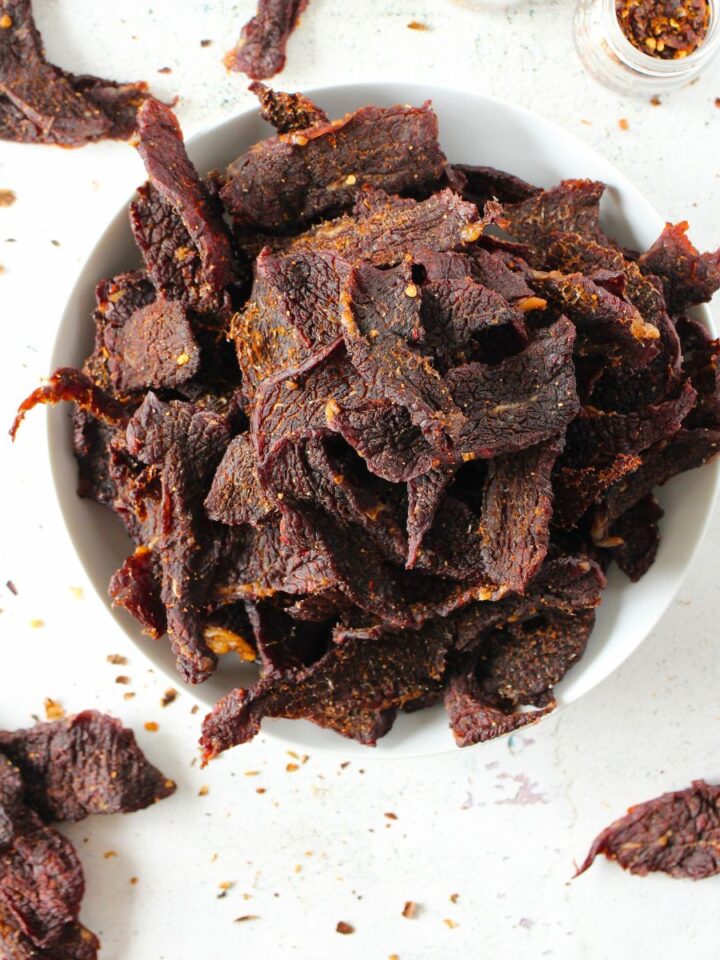 a bowl of homemade carnivore jerky in a bowl with scattered pieces of keto jerky lying around the bowl