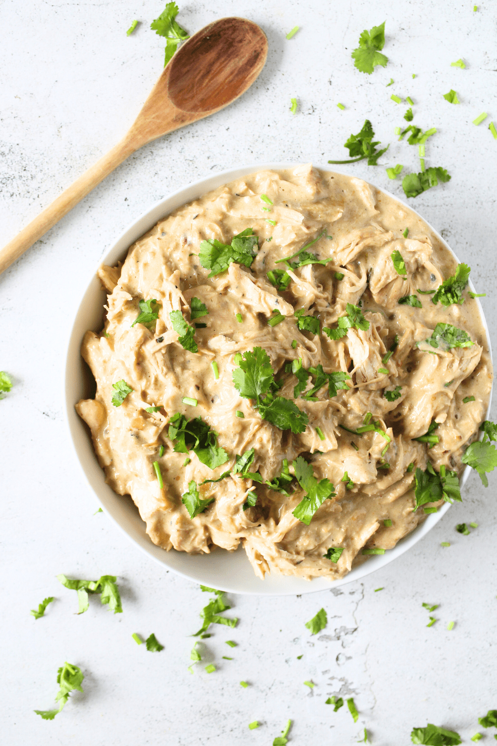 top view of a bolw of instant pot creamy salsa verde chicken with fresh parsley and a wooden spoon