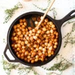keto creamed pearl onions in a cast iron skillet with a wooden spoon and fresh thyme