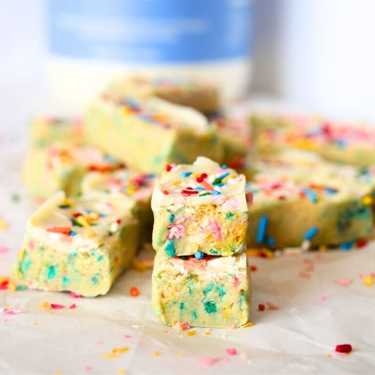 a PSMF Birthday Cake Protein bar cut in half with egg white protein powder in the background by Naked Nutrition