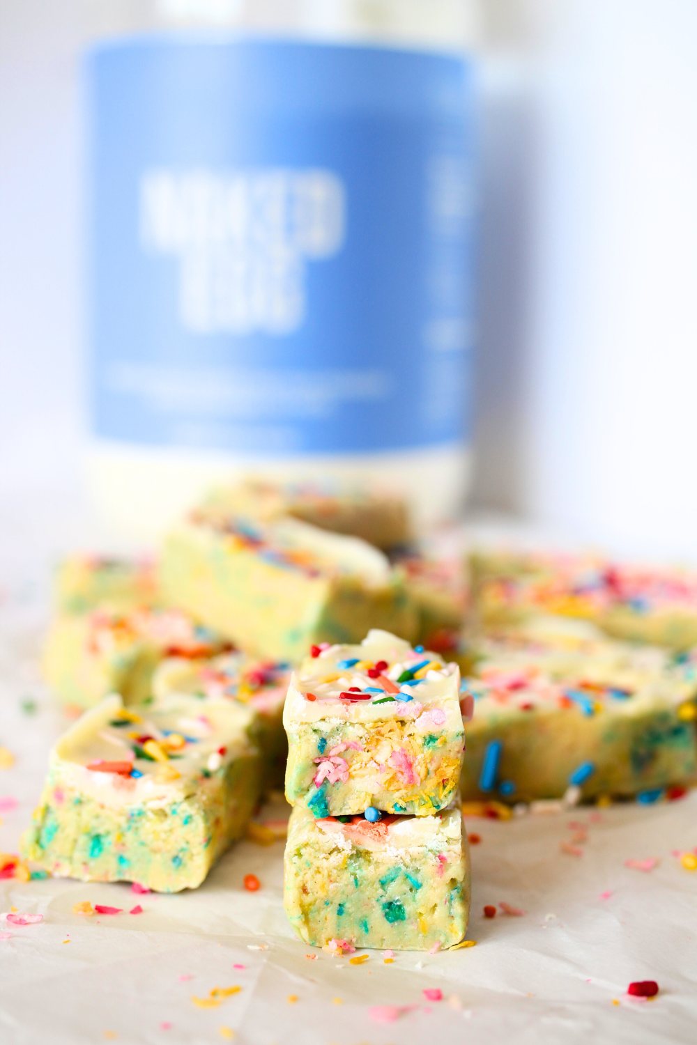 a PSMF Birthday Cake Protein bar cut in half with egg white protein powder in the background by Naked Nutrition