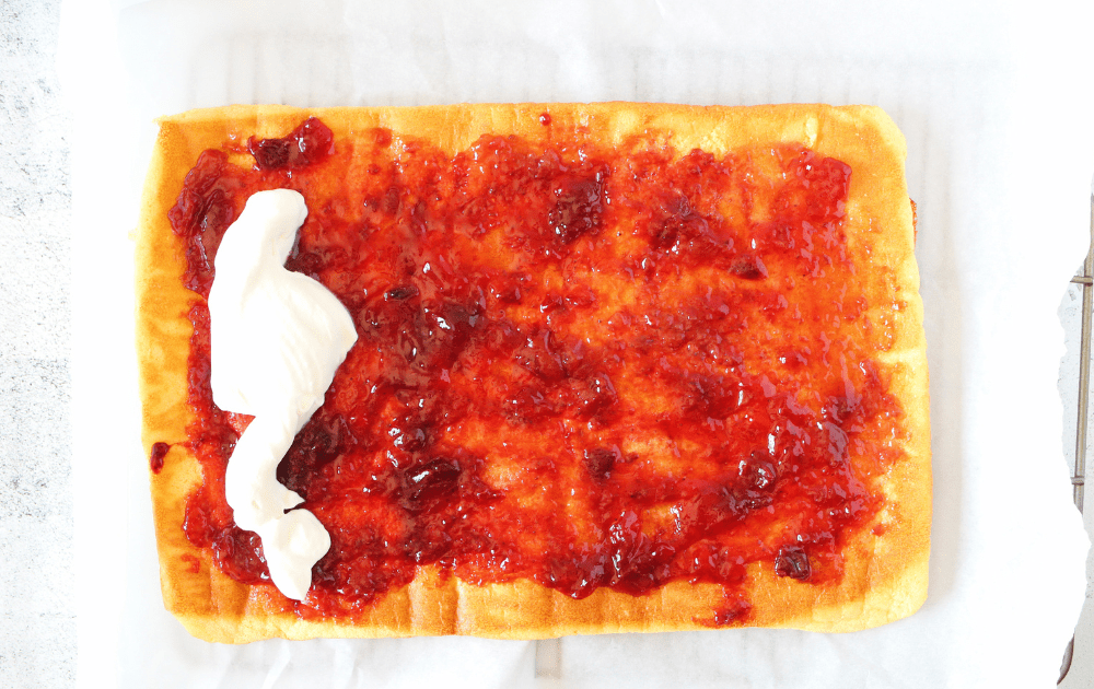 top view of keto roll cake unrolled with a layer of sugar-free jam and sugar-free cream filling before being rolled