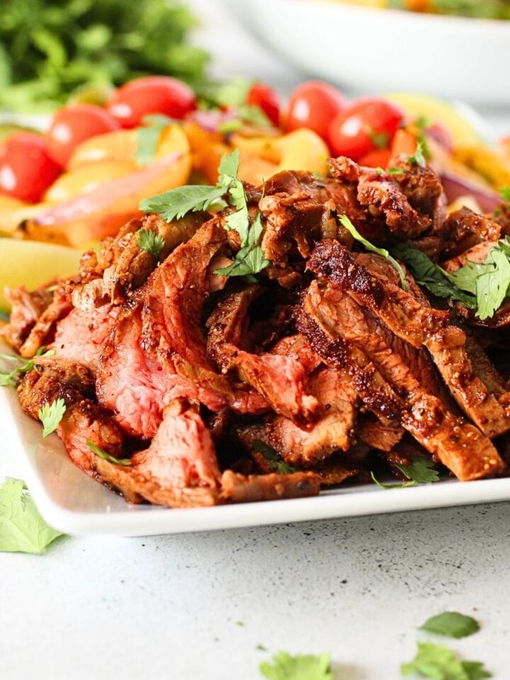 front view of keto sheet pan steak fajitas on a serving dish with roasted peppers and cilantro in the background