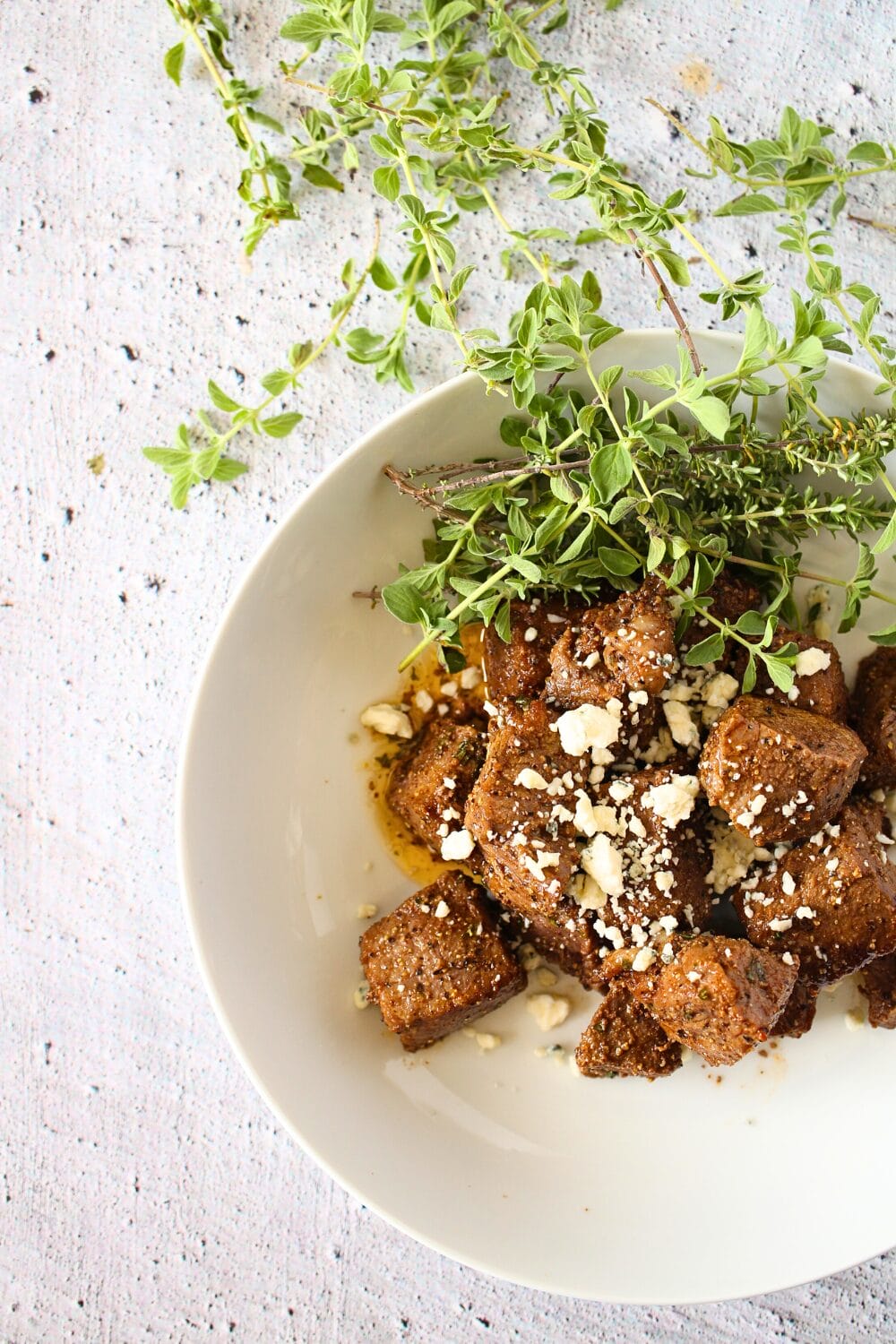 air fryer carnivore steak bites with crumbled blue cheese in a white bowl with crumbled blue cheese on top