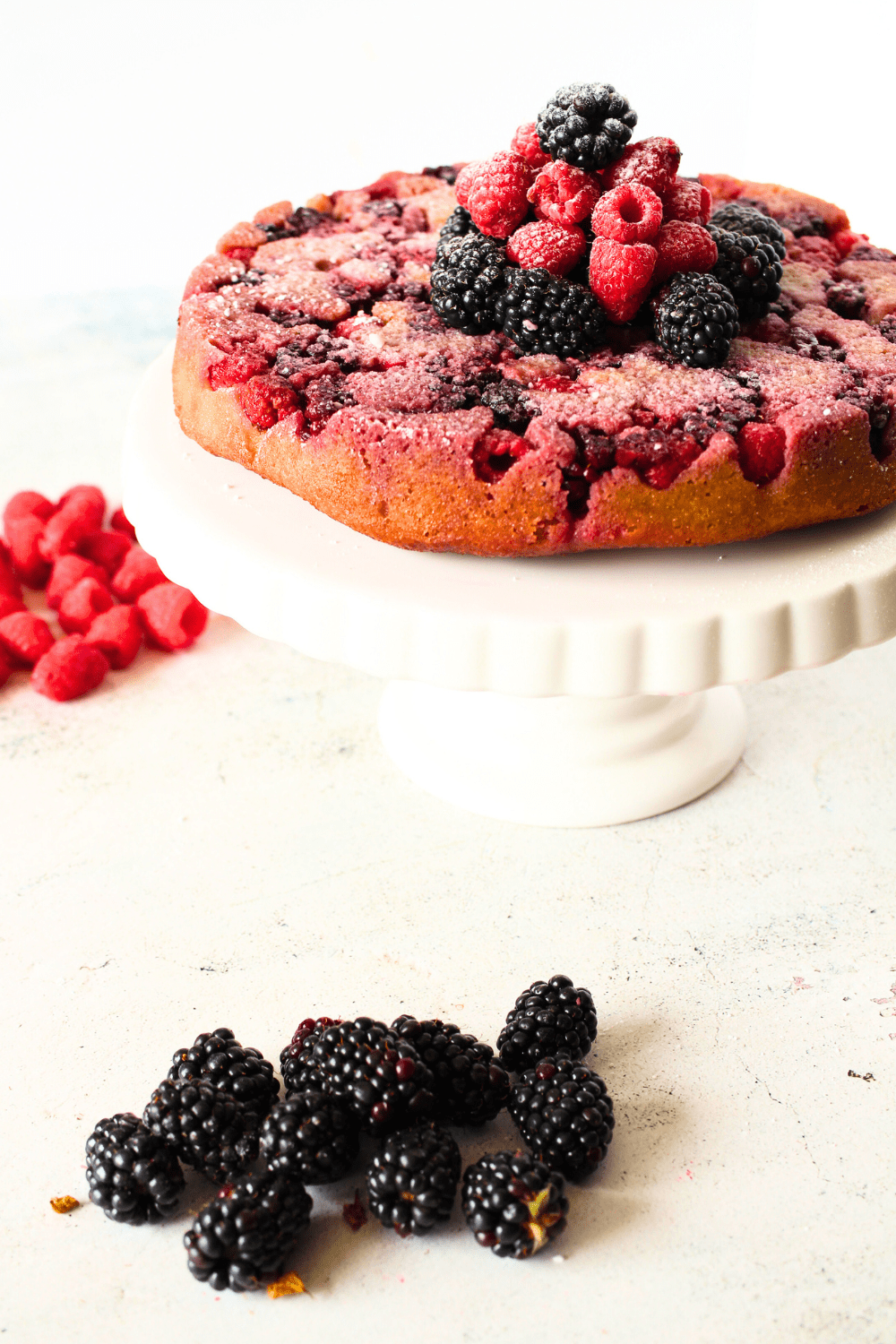 low carb blackberry cake on a cake stand with blackberries and rapsberries