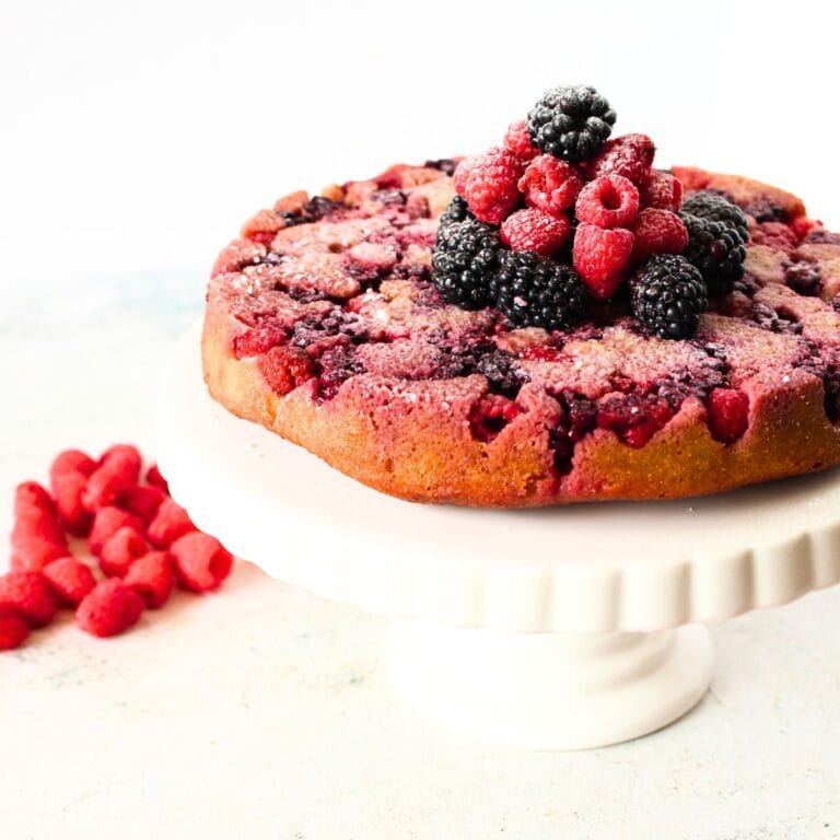 low carb blackberry cake on a cake stand with blackberries and rapsberries