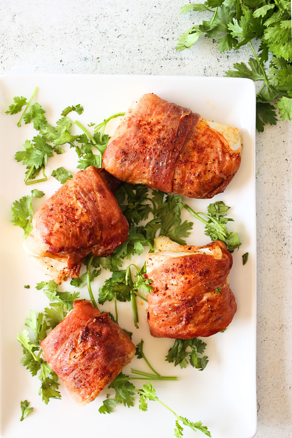 PSMF Air Fryer baked cod wrapped in prosciutto on a serving platter with fresh herbs