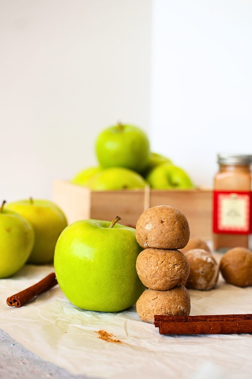 low carb protein bars made into balls and flavoured like apple pie.  A green apple and a cinnamon stick are scattered about the bites