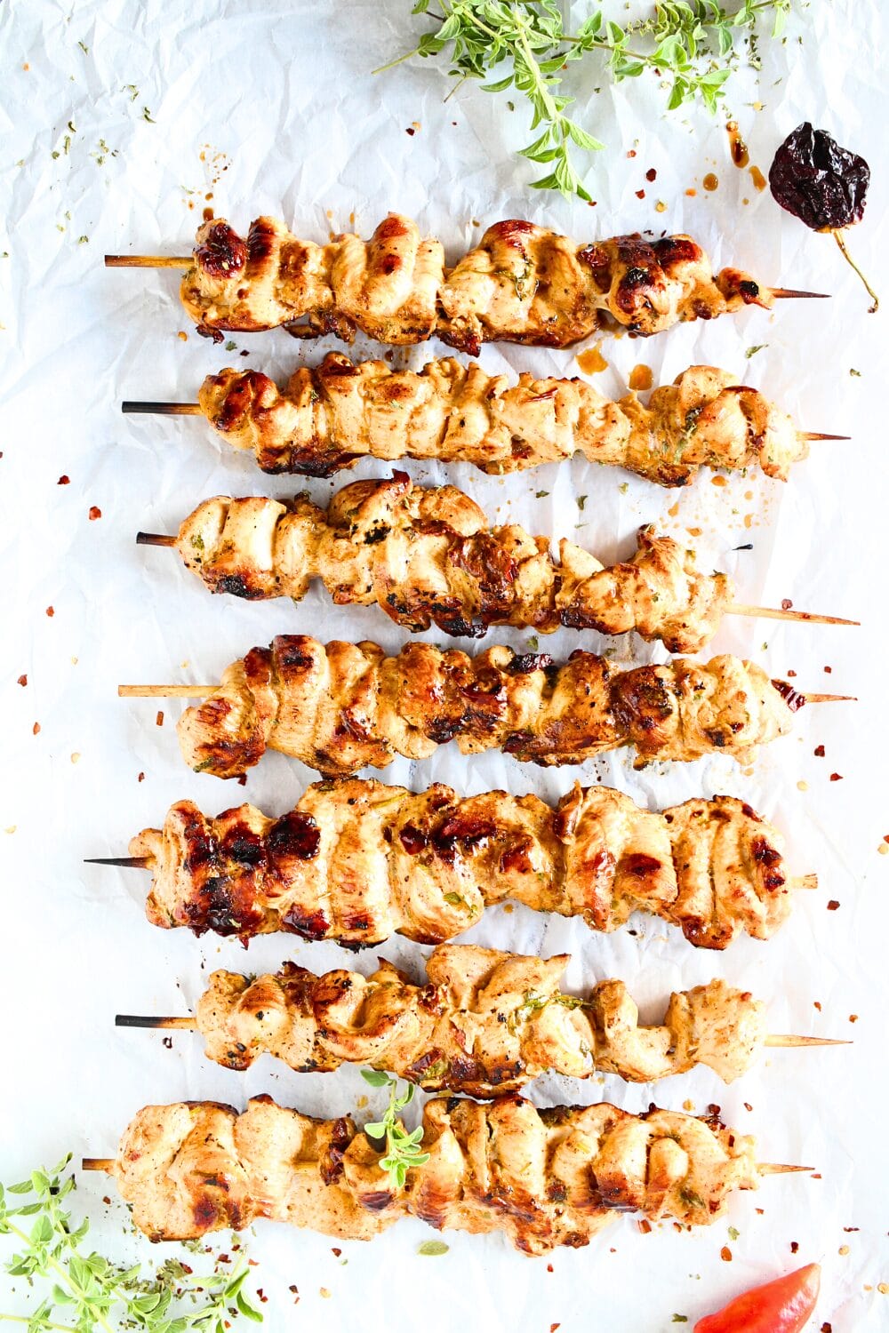 keto chicken skewers lined up with fresh herbs and chipotle peppers in the background