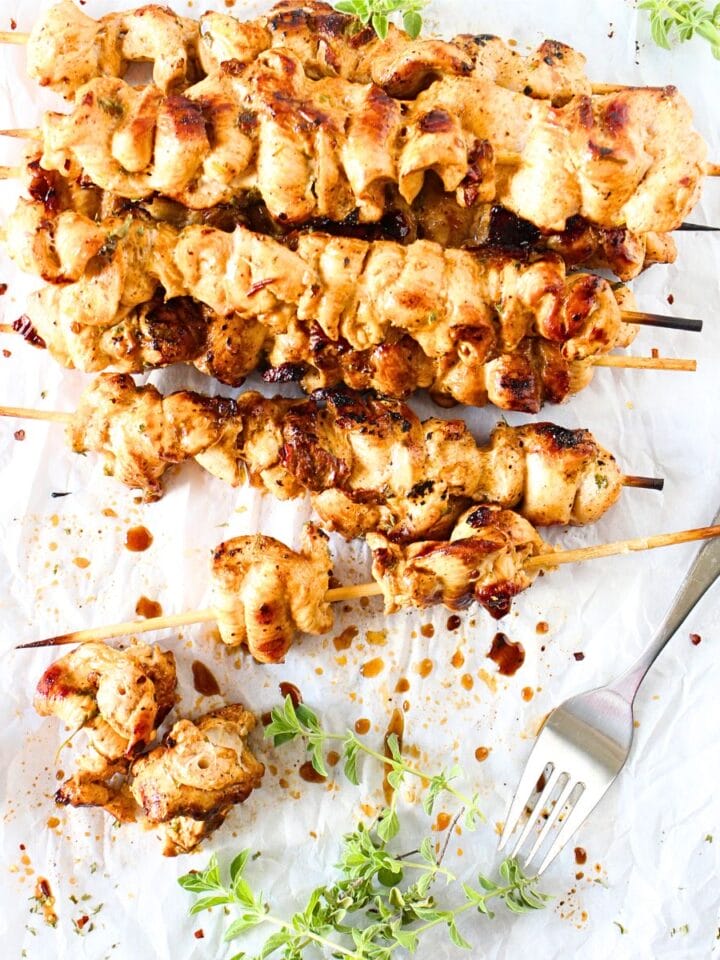 top view of high protein chipotle chicken skewers wtih fresh herbs scattered about