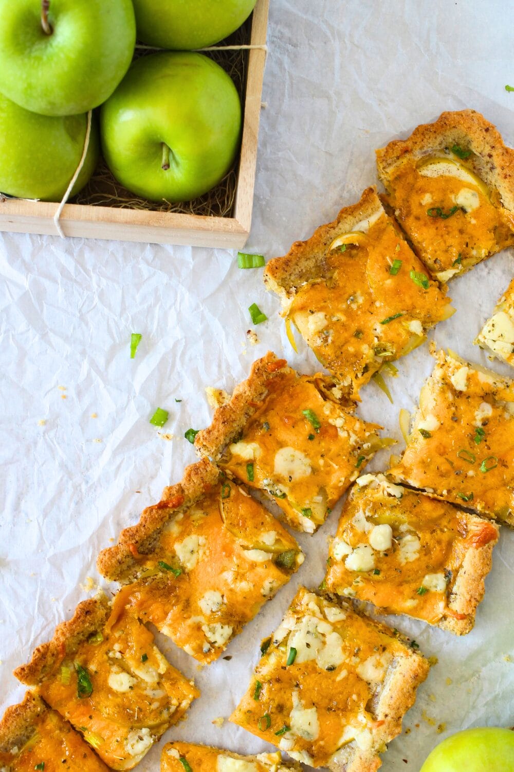 top view of keto cheddar apple tart divided into sections with fresh green apples in a basket.
