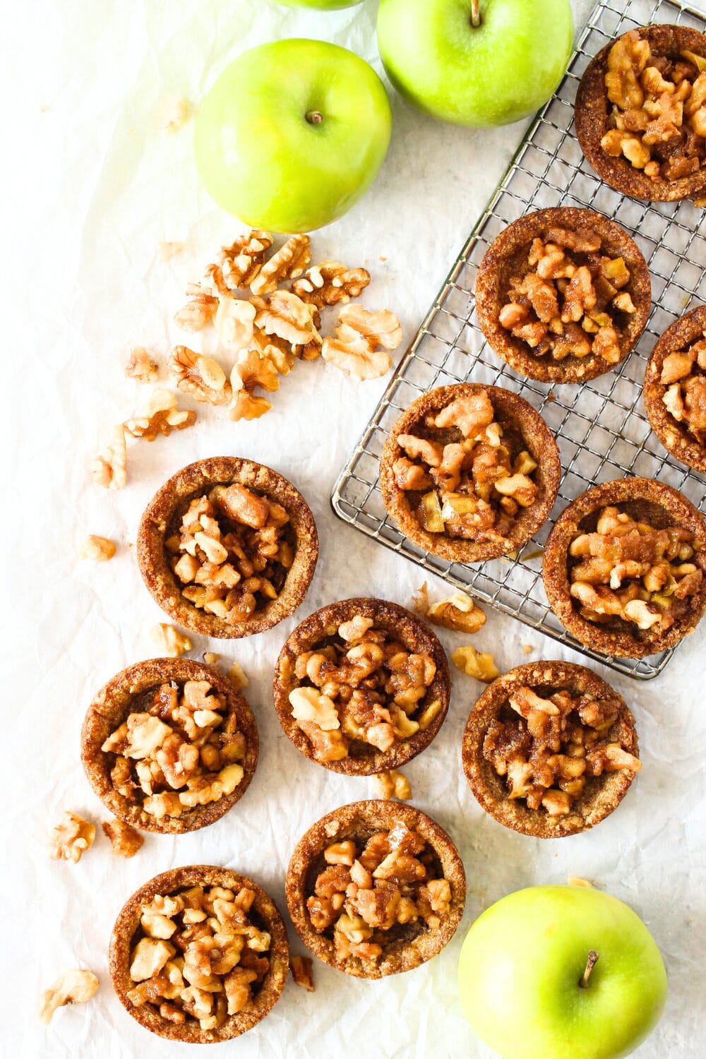 top view of keto mini apple pies made in cookie cups with green apples and nuts scattered around the sugar-free apple cookie cups