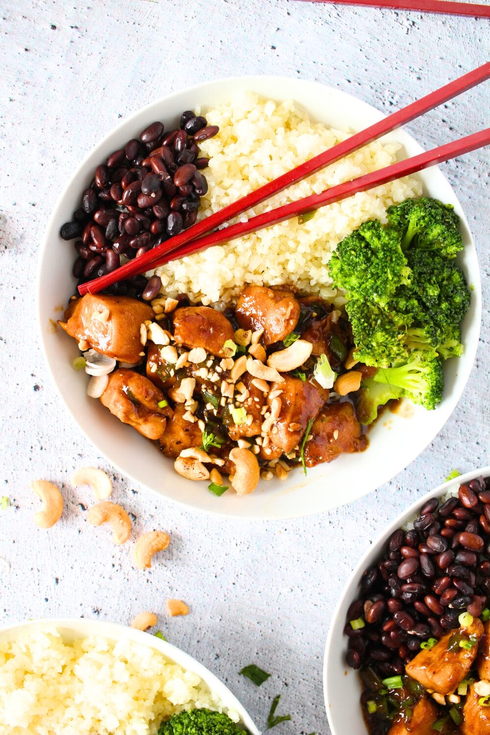 a bowl of keto cashew chicken with broccoli, riced cauliflower and black soybeans with chopsticks