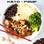 a bowl of keto cashew chicken with broccoli, riced cauliflower and black soybeans with chopsticks