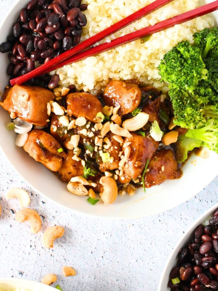 a bowl of keto cashew chicken with broccoli, riced cauliflower and black soybeans with chopsticks