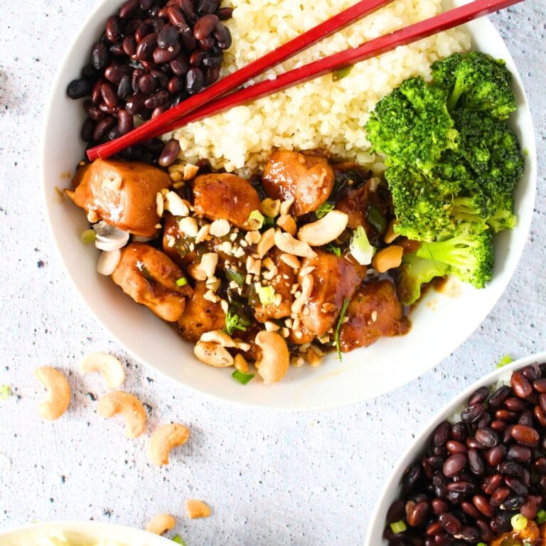 a bowl of keto cashew chicken with broccoli, riced cauliflower and black soybeans with chopsticks