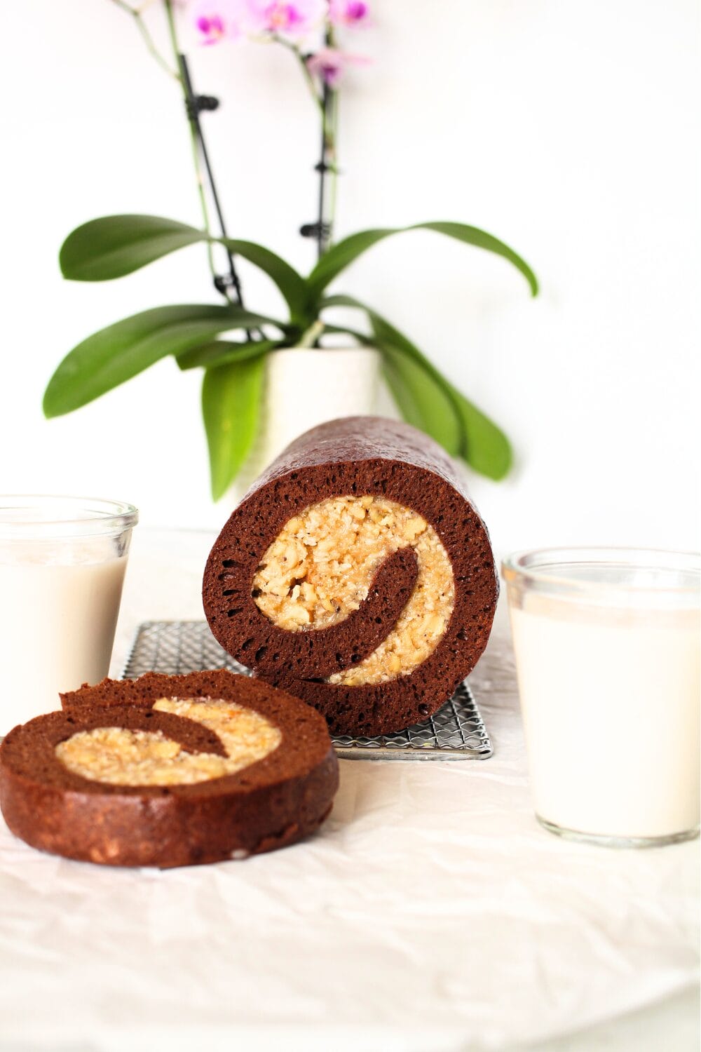 keto German chocolate roll cake with sugar-free pecan coconut filling, with glasses of almond milk and an orchid in the background