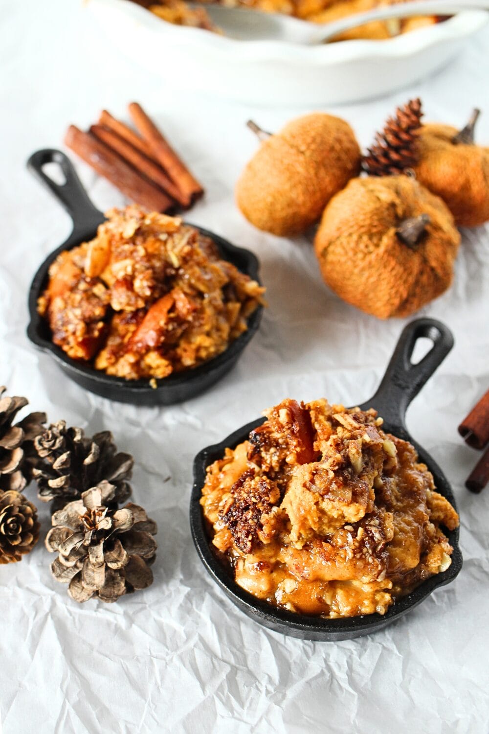 2 servings of keto pumpkin crisp in cast iron bowls with decorative pumpkins and cinnamon sticks
