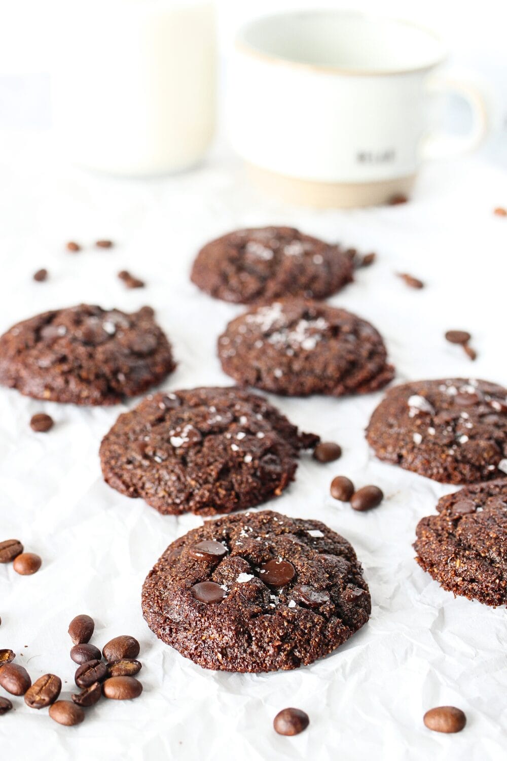 keto chocolate cookies with espresso beans scattered about and a glass of almond milk in the background