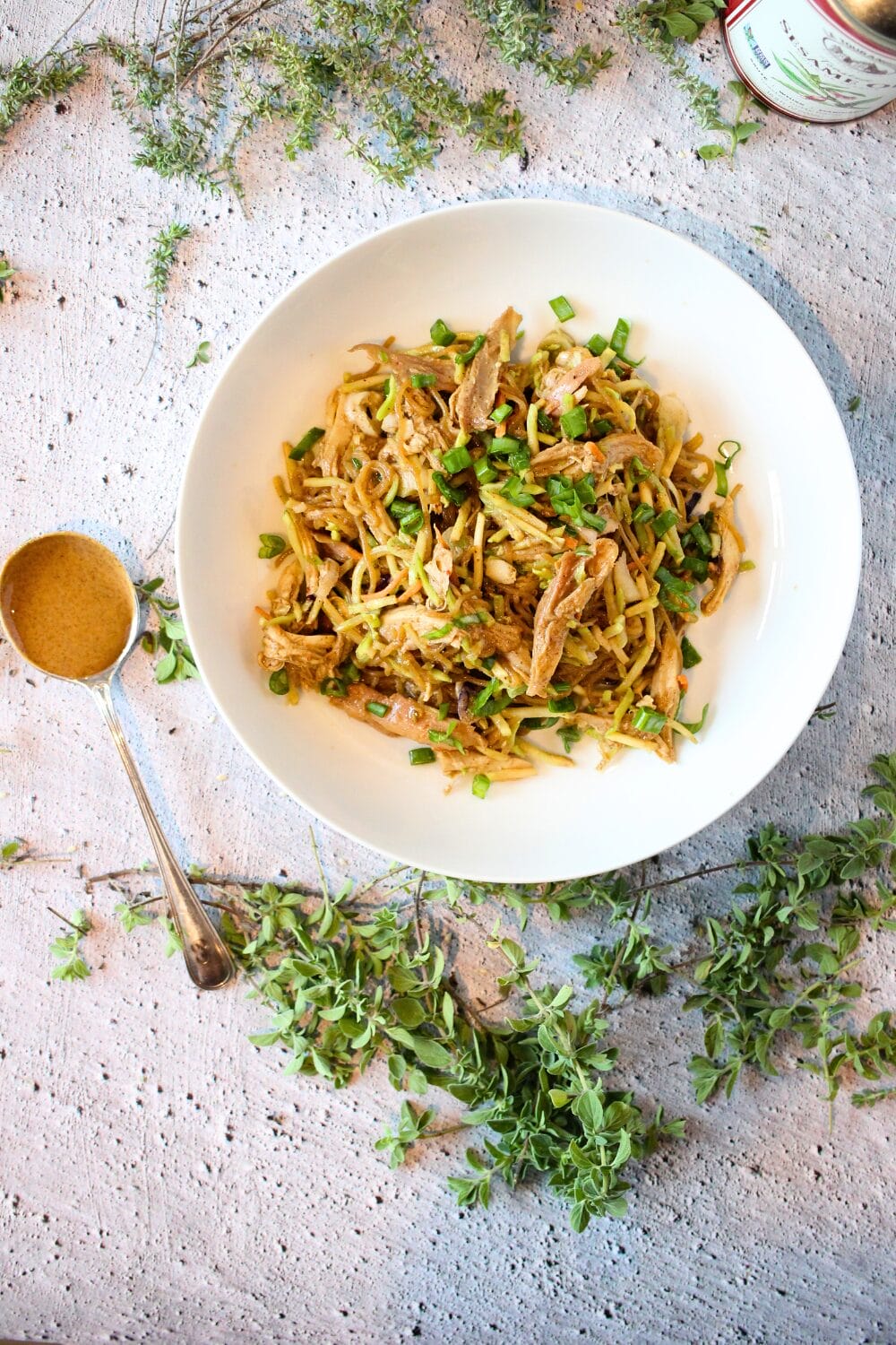 top view of a white bowl filled with keto warm almond butter noodles with chicken and sliced green onion with a spoon of almond butter to the side.