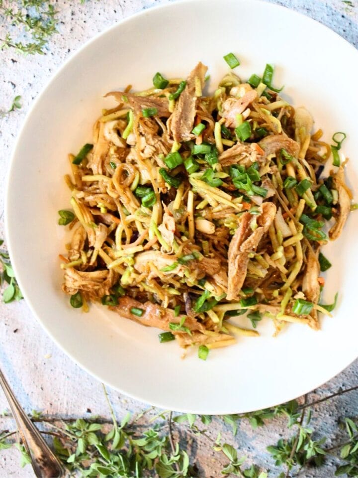 top view of a white bowl filled with keto warm almond butter noodles with chicken and sliced green onion with a spoon of almond butter to the side.