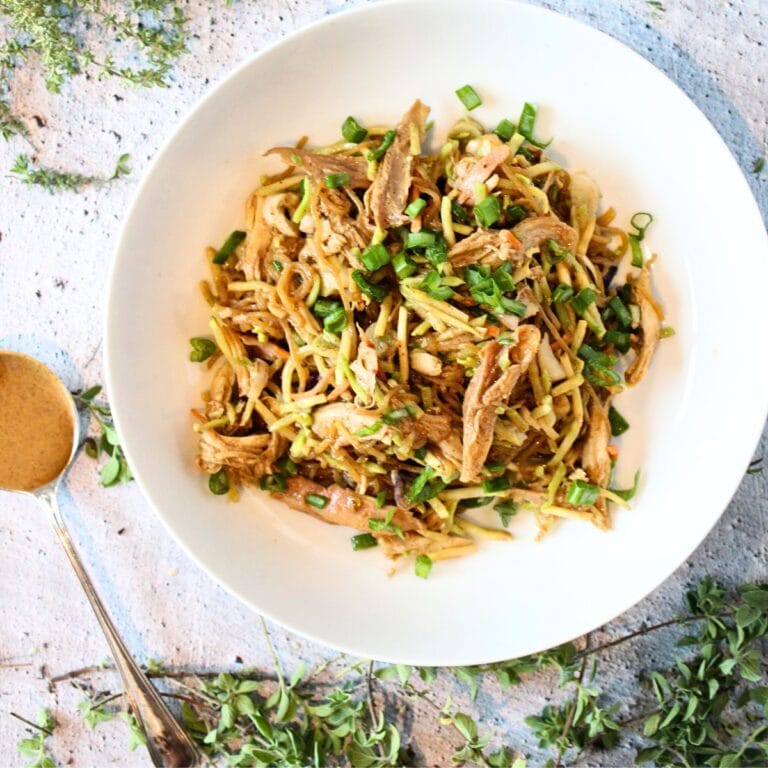 top view of a white bowl filled with keto warm almond butter noodles with chicken and sliced green onion with a spoon of almond butter to the side.