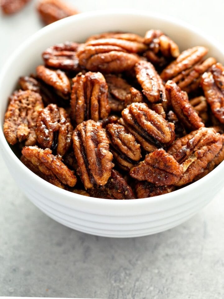 a bowl of keto candied bourbon nuts in a white bowl with keto candied nuts scattered about