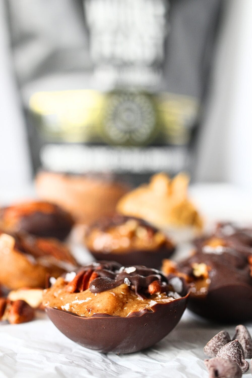 front view of keto roasted pecan chocolate clusters in a chocolate cup with collagen protein powder in the background