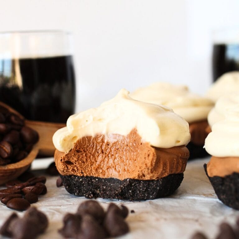 front view of a keto no-bake mini mocha cheesecake with espresso shots and sugar-free chocolate in the background