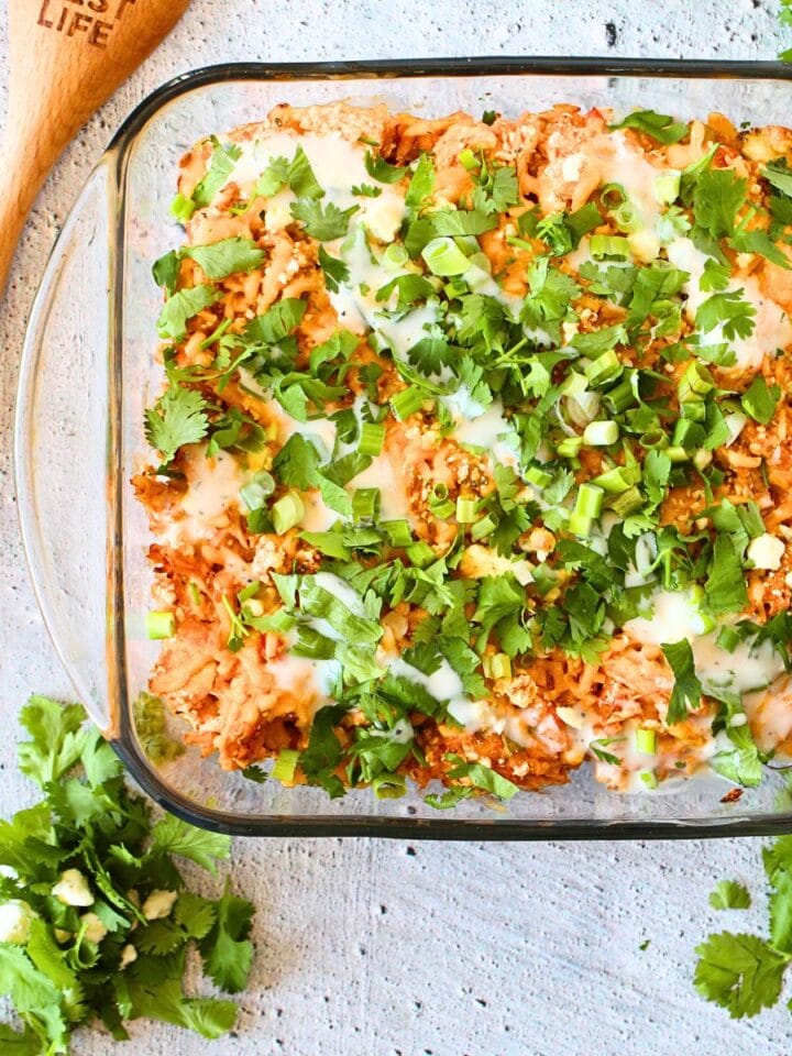 top view of a healthy chicken casserole wtih hot sauce and cilantro on top and a wooden spoon on the side