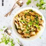 top view of high protein slow cooker sweet cilantro chicken in a bowl with large spoons and fresh cilantro surrounding bowl.