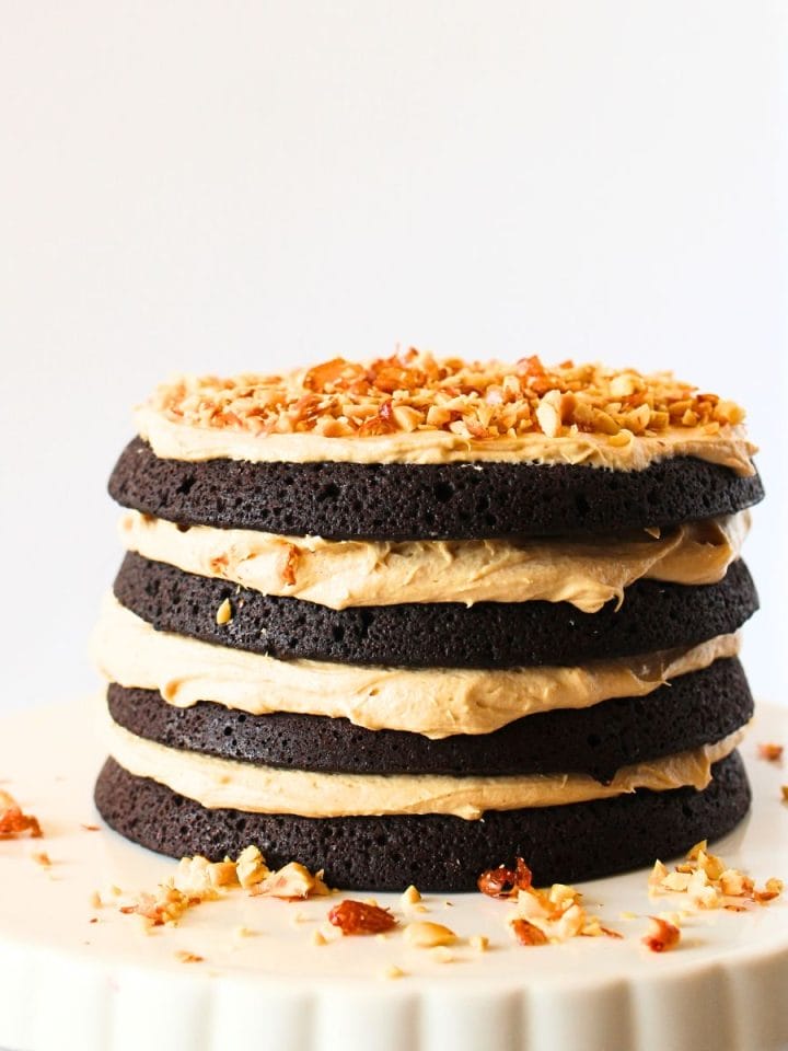 front view of a keto chocolate cake with peanut butter frosting and chopped peanuts on top on a serving platter