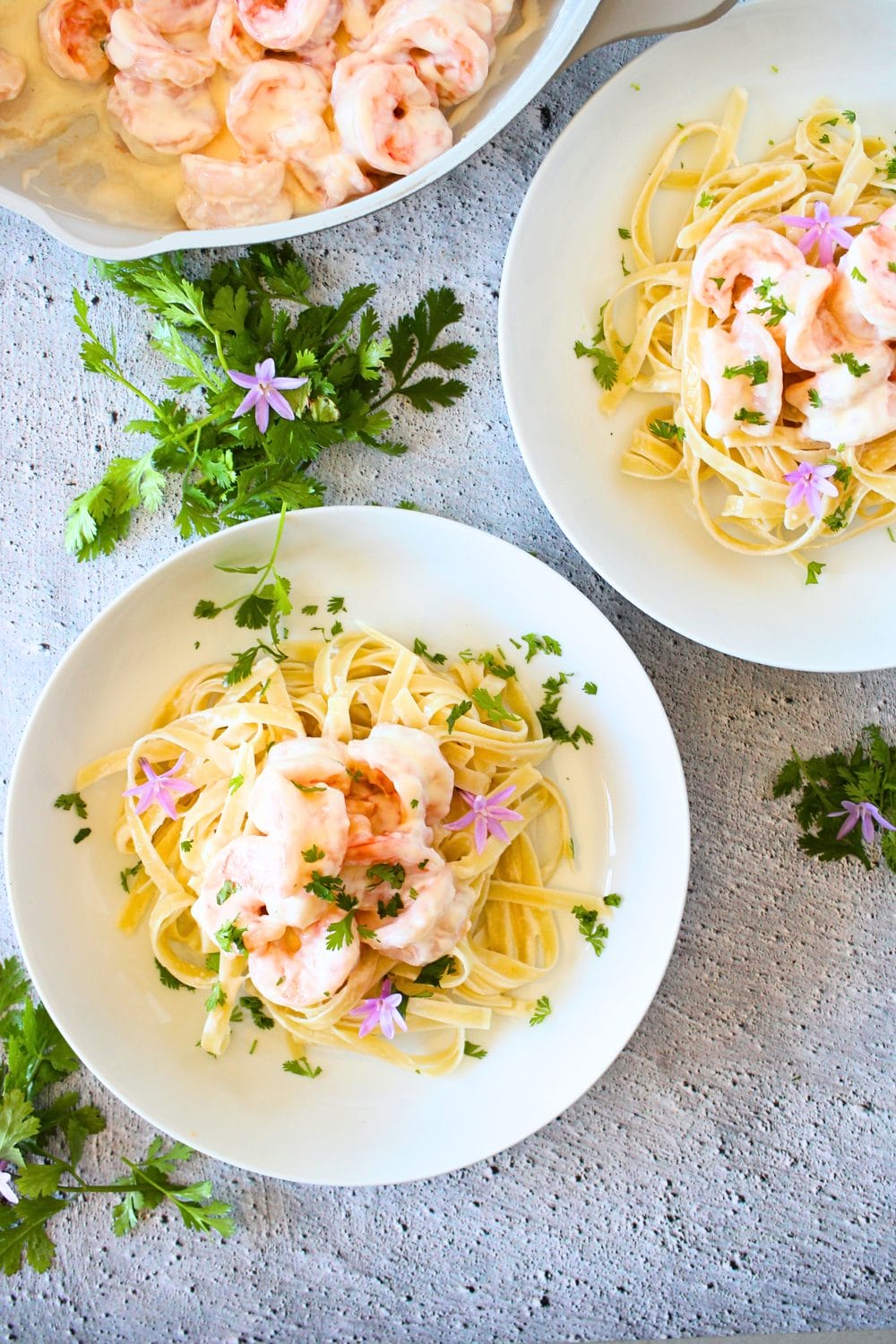 top view of 2 bowls filled with creamy keto shrimp Parmesan Linguini and fresh herbs scattered about