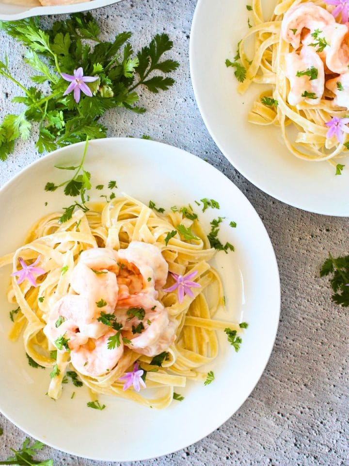 top view of 2 bowls filled with creamy keto shrimp Parmesan Linguini and fresh herbs scattered about