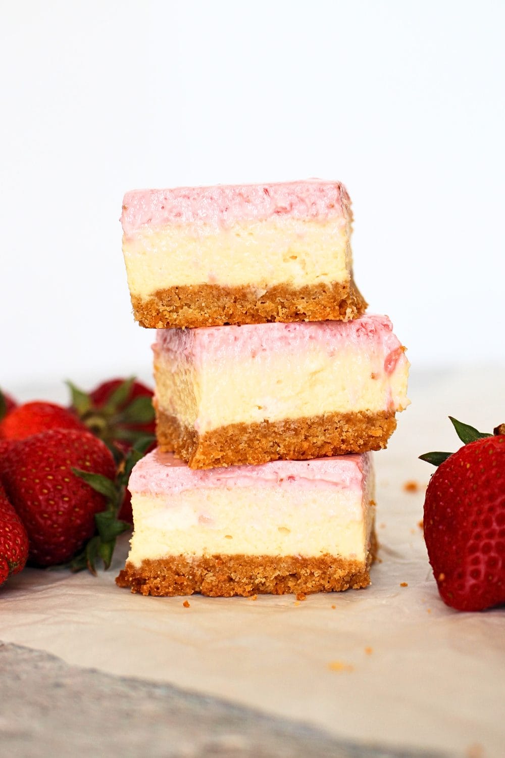 front view of 3 stacked  keto strawberry cheesecake bar with a slice strawberry