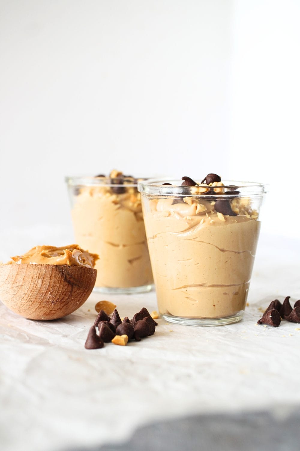 front view of two cups filled with high protein vegan peanut butter mousse with peanut butter and sugar-free chocolate chips scattered about