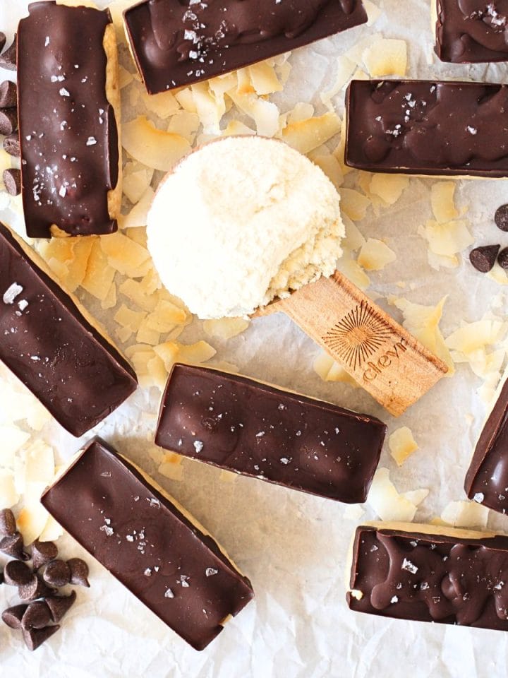 top view of keto almond joy protein bars with a scoop of protein powder and sugar-free chocolate chips scattered about