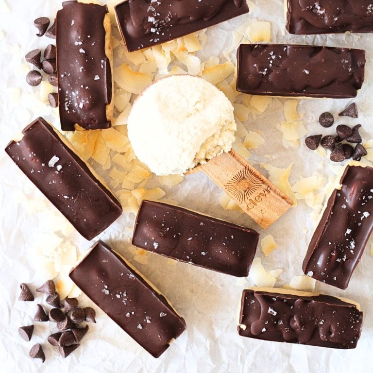 top view of keto almond joy protein bars with a scoop of protein powder and sugar-free chocolate chips scattered about