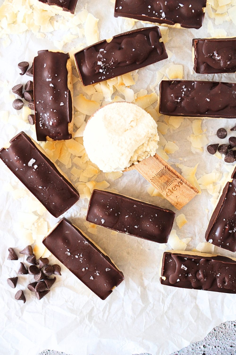 top view of keto almond joy protein bars with a scoop of protein powder and sugar-free chocolate chips scattered about