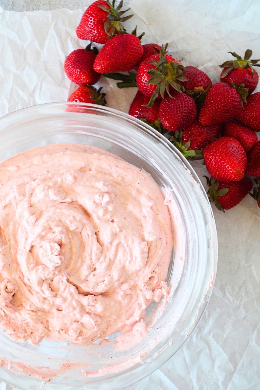 top view of a glass bowl with keto fluffy strawberry mousse and some fresh strawberries scattered around the bowl