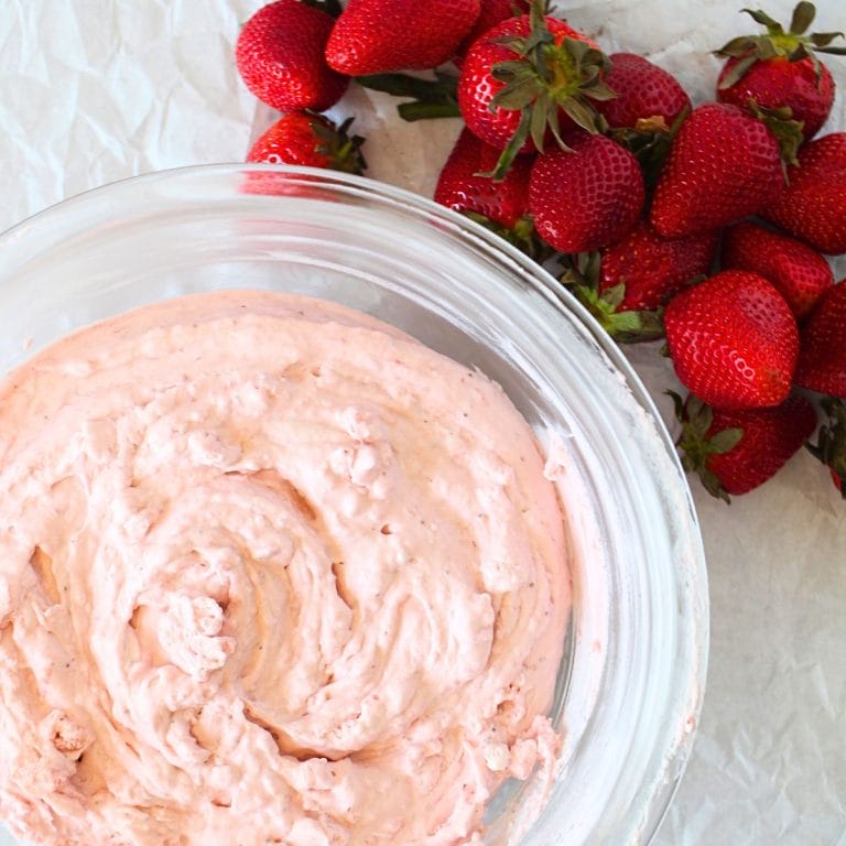 top view of a glass bowl with keto fluffy strawberry mousse and some fresh strawberries scattered around the bowl