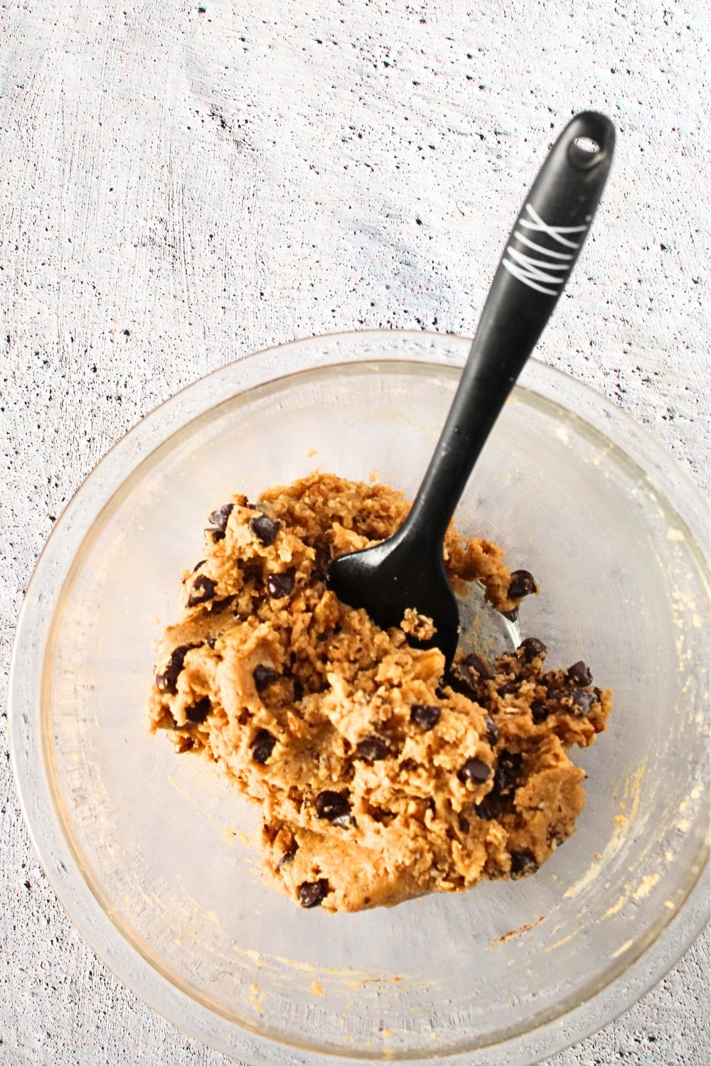 top view of a bowl filled with keto giant monster collagen cookie ingredients and a spatula that folded in the sugar-free chocolate chips