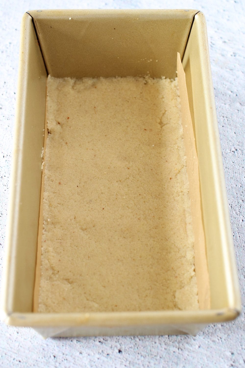top view of a loaf pan lined with parchment paper and the keto millionaire bottom crust made of almond flour and pea protein powder