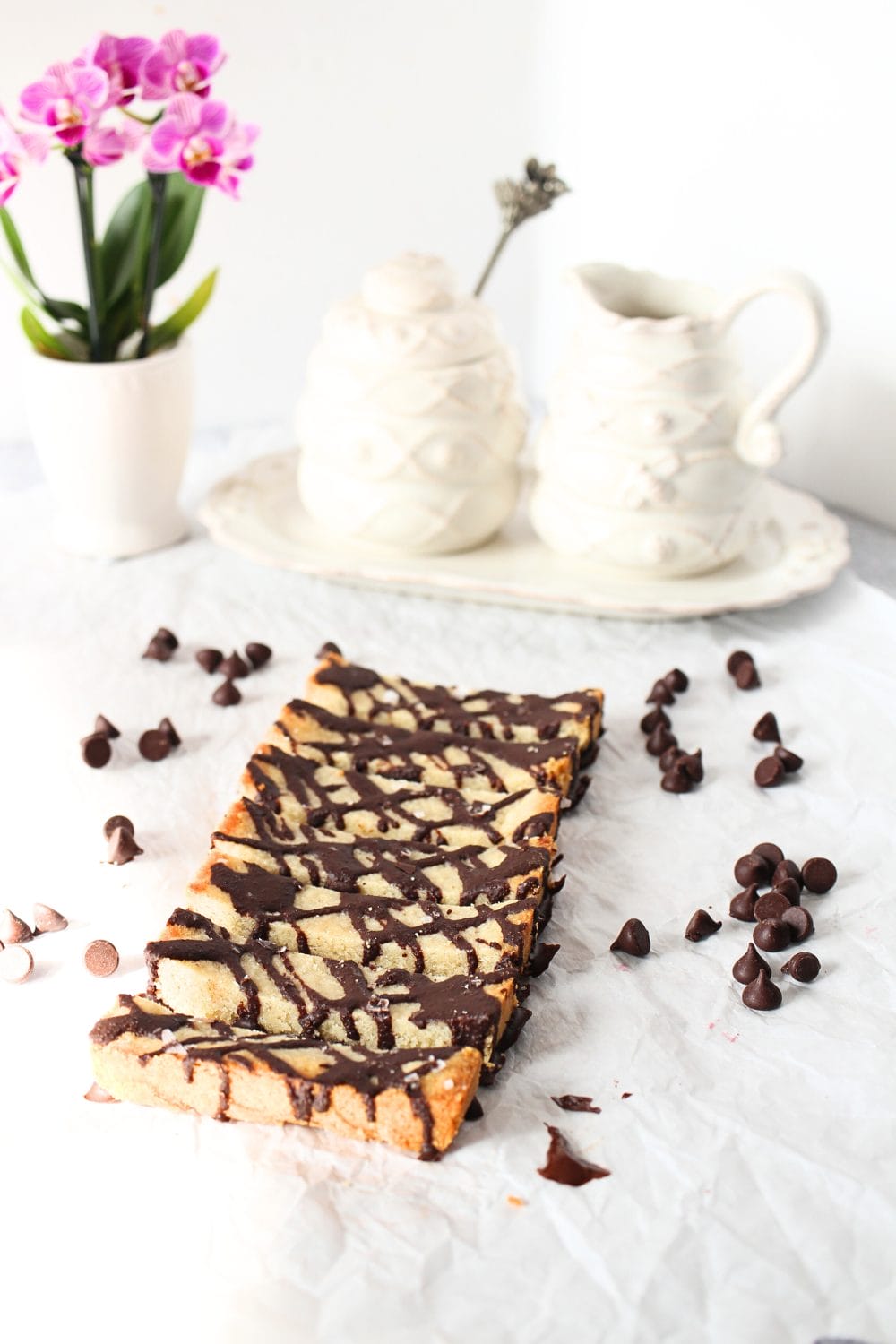 front view of keto shortbread cookie bars with sugar-free chocolate drizzle, chocolate chips and an orchid plant for decoration