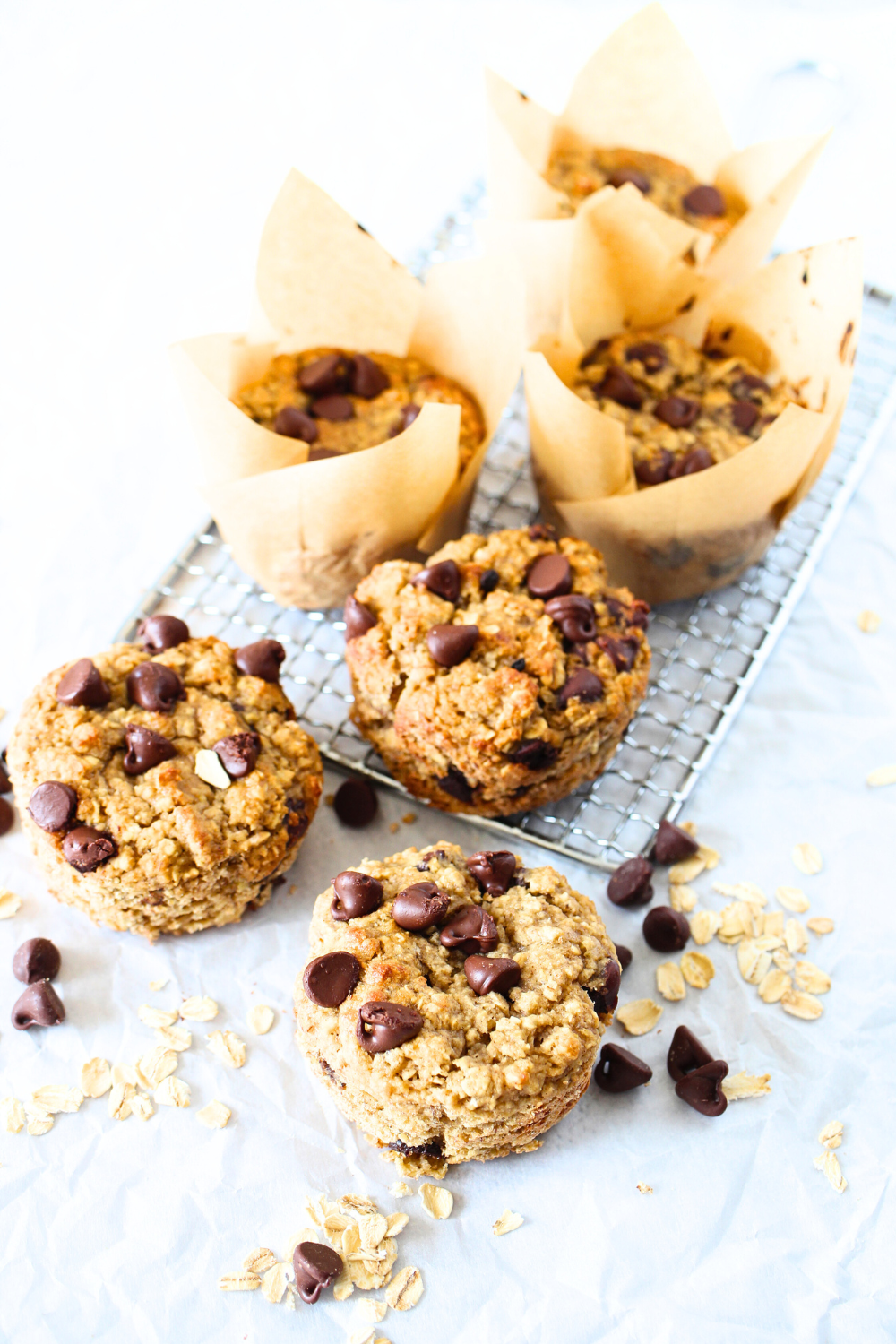 Easy Nut-Free & Gluten-Free Chocolate Chip Banana Oat Muffins that have been baked and are cooling with chocolate chips and oats scattered about